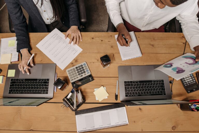 Wann sollten bestimmte Unternehmensaufgaben ausgelagert werden? Unternehmensaufgaben auslagern – Team arbeitet mit Laptops und Unterlagen am Schreibtisch
