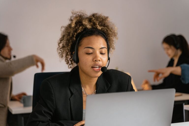 Kaltakquise – Mitarbeiterin mit Headset telefoniert im Büro am Laptop