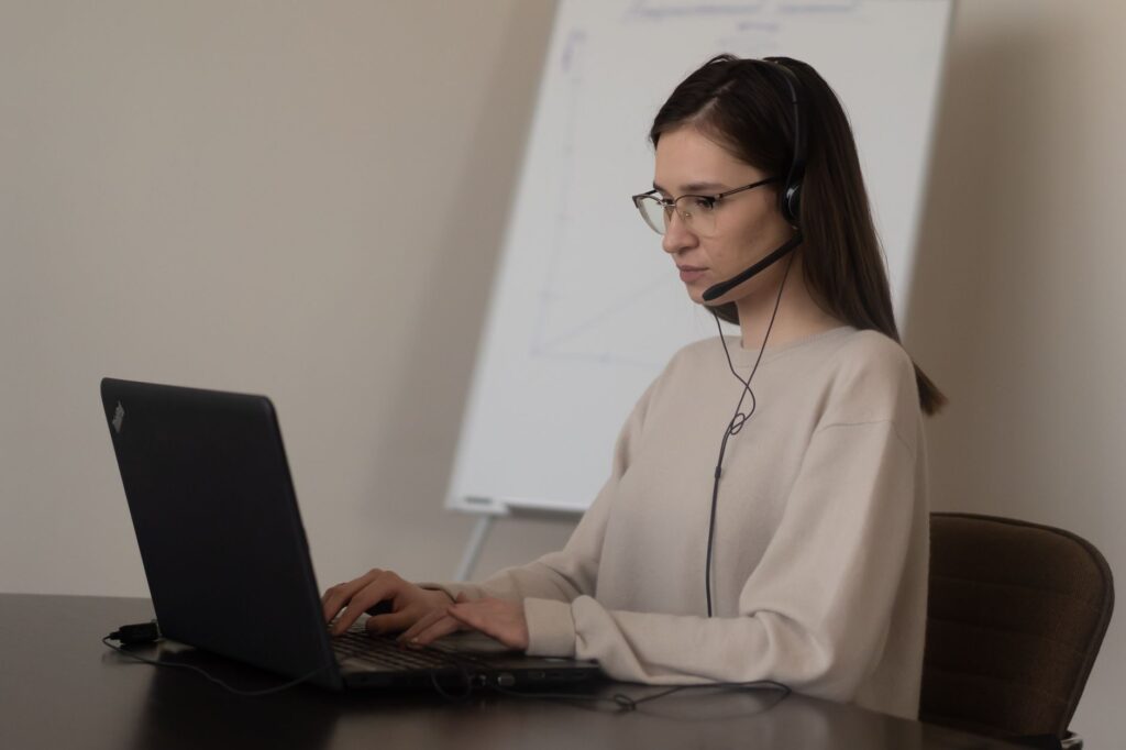 Kaltakquise – Frau mit Headset bereitet ein Verkaufsgespräch am Laptop vor
