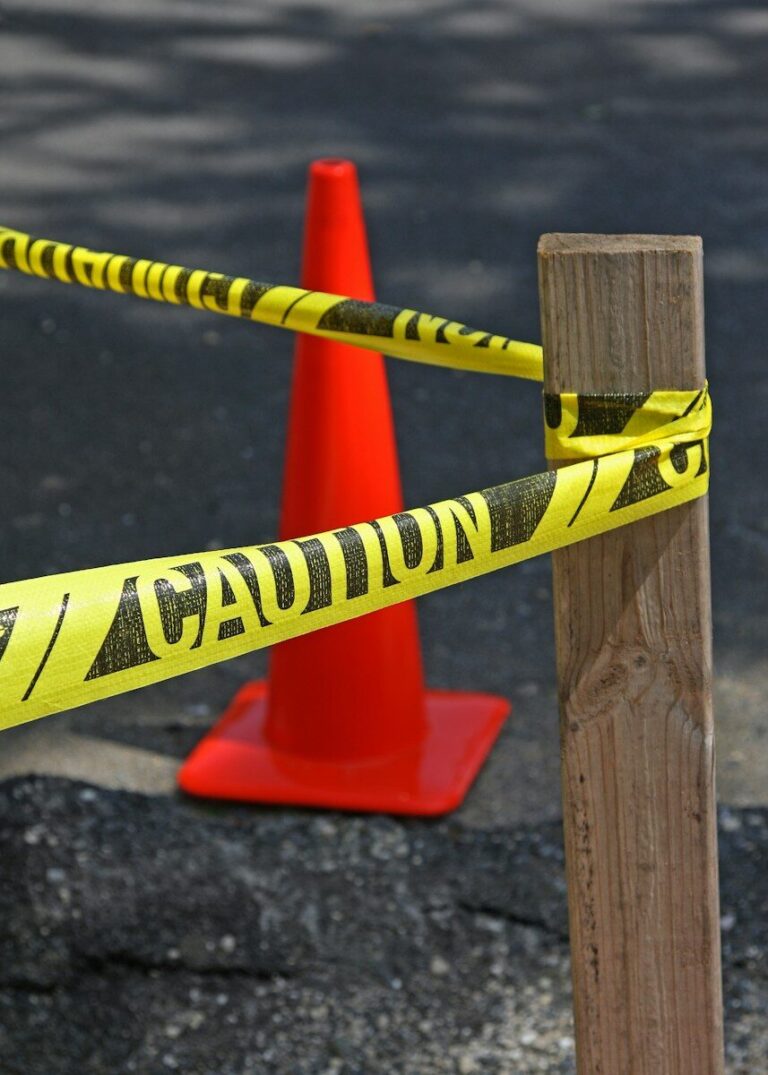 Yellow caution tape tied to wooden post, red cone